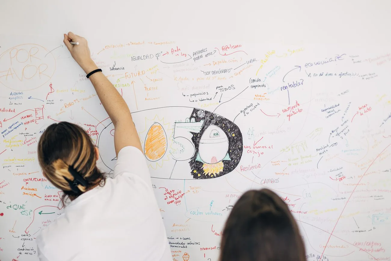 Participante escribiendo sobre una pizarra llena de esquemas e ideas