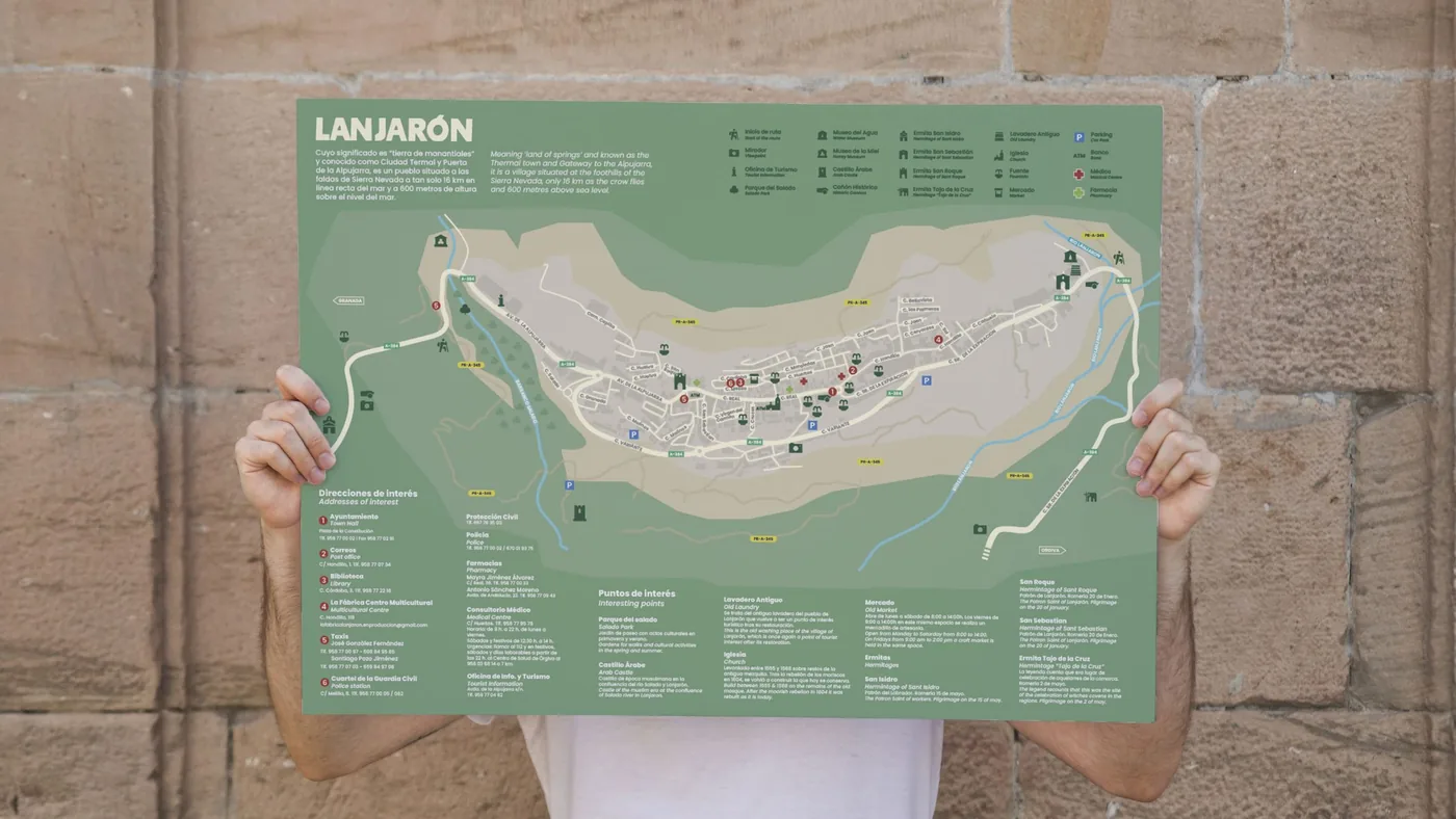 Persona sosteniendo el mapa turístico de Lanjarón desplegado frente a un muro de piedra
