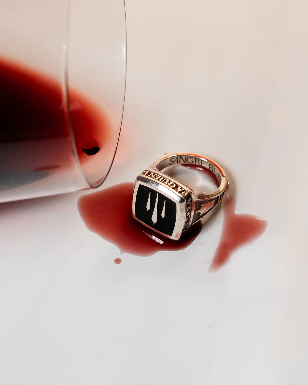 Anillo de sello junto a una copa de vino tinto derramada