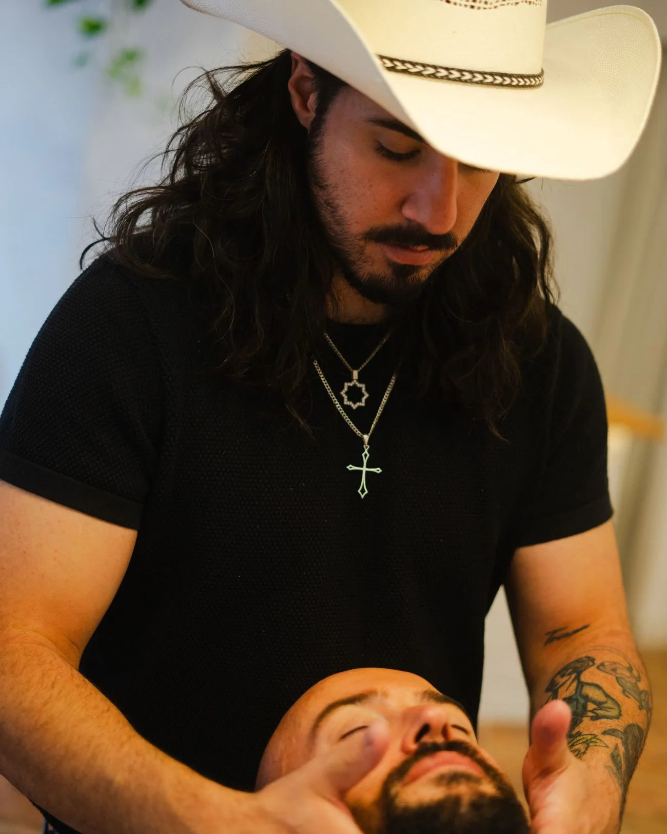 Barbero con sombrero vaquero dando un masaje facial a un cliente en la barbería