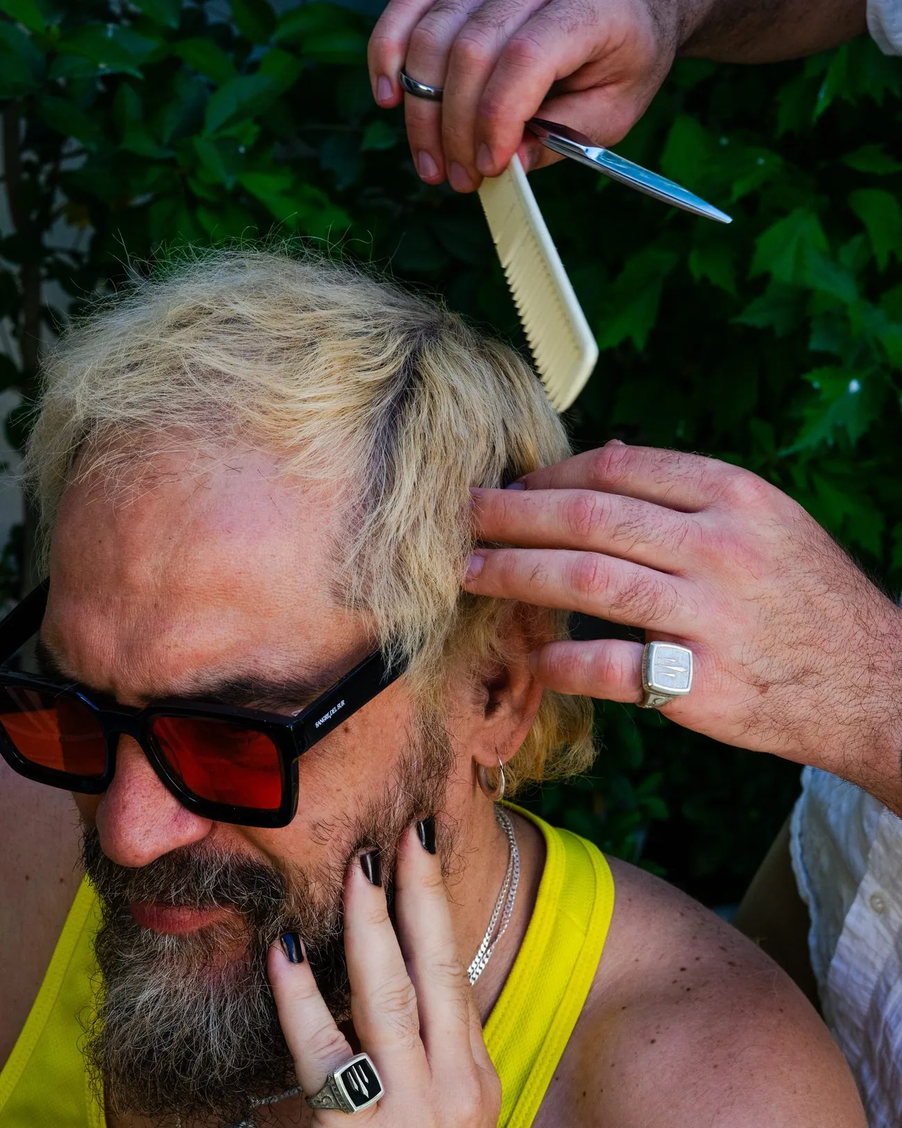 Tony Moreno, con gafas de sol rojas, mientras le arreglan el pelo con peine y navaja