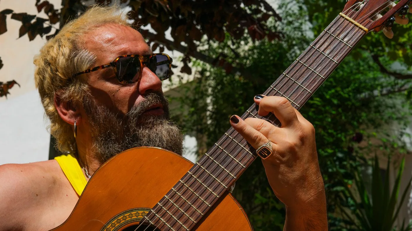 Tony Moreno, con gafas de sol, tocando la guitarra española en un patio con vegetación