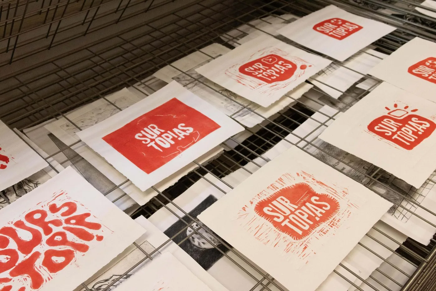Grabados en rojo con el logotipo de Surtopías secándose en un tendedero