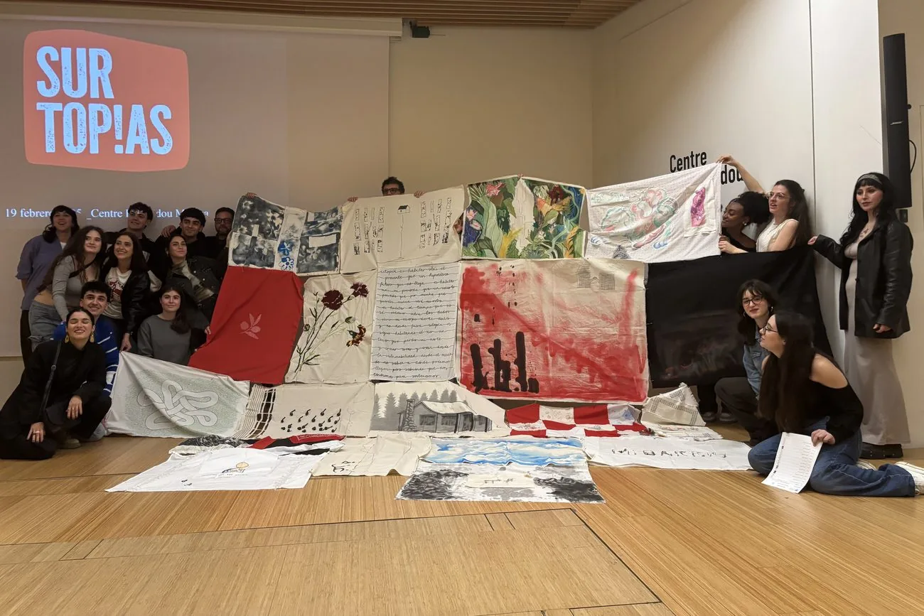 Grupo de participantes junto a un gran tapiz colectivo con el logotipo de Surtopías proyectado al fondo