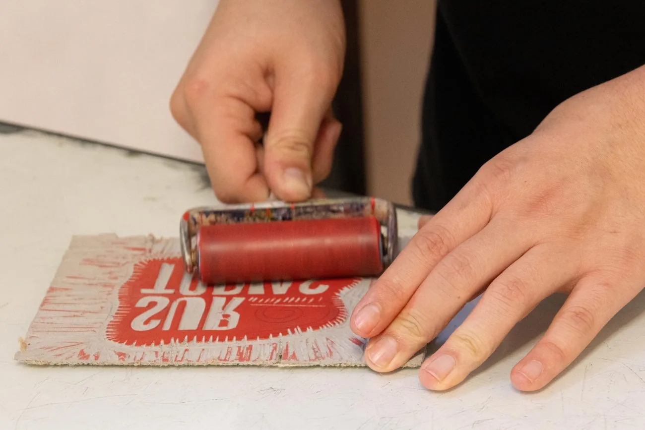 Manos entintando con un rodillo rojo una matriz de grabado de Surtopías