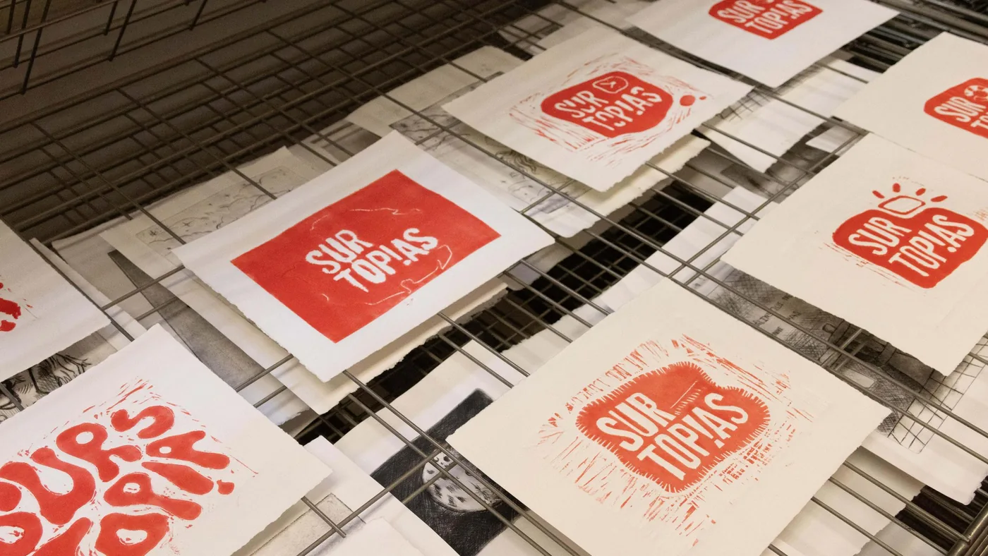 Grabados en rojo con el logotipo de Surtopías secándose en un tendedero